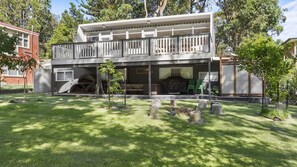 Une maison à deux étages dotée d’un balcon, d’un espace extérieur aménagé et couvert, et d’une pelouse bien entretenue agrémentée de rochers.