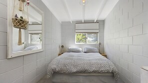 Ein Schlafzimmer mit einem Bett, einem Fenster, einem Spiegel und einer Wanddeko aus Makramee.