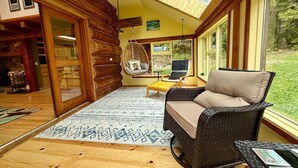 Een blokhutinterieur met een groot raam, een hangstoel en een rieten bank.
