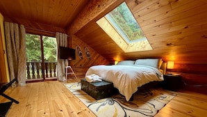 Een gezellig slaapkamer met een bed, een tafeltje, een televisie en een raam met uitzicht op bomen.