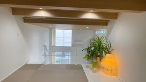 Ein geräumiger, hell erleuchteter Innenraum mit einer Treppe, die in ein Obergeschoss führt, einer Zimmerpflanze und einer Stehlampe.