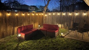 A backyard with a wooden fence, two red cushioned chairs, a wicker table, and string lights. - Prime Location-  Cozy 2-bedroom house in serene Arlington with AC (Arlington)