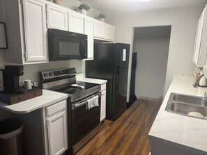 A modern kitchen with white cabinetry, a black microwave, a black refrigerator, a black stove, and a coffee maker. - Prime Location-  Cozy 2-bedroom house in serene Arlington with AC (Arlington)