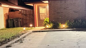 A residential building with a brick facade, a wooden fence, and a driveway leading to a door. - Prime Location-  Cozy 2-bedroom house in serene Arlington with AC (Arlington)