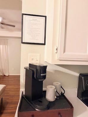 A Keurig coffee maker on a tray with two disposable cups, a framed welcome sign, and a white door in a hotel room. - Prime Location-  Cozy 2-bedroom house in serene Arlington with AC (Arlington)