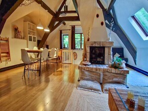 Um loft espaçoso com teto alto, vigas de madeira aparentes, lareira e área de jantar com cadeiras e mesa.
