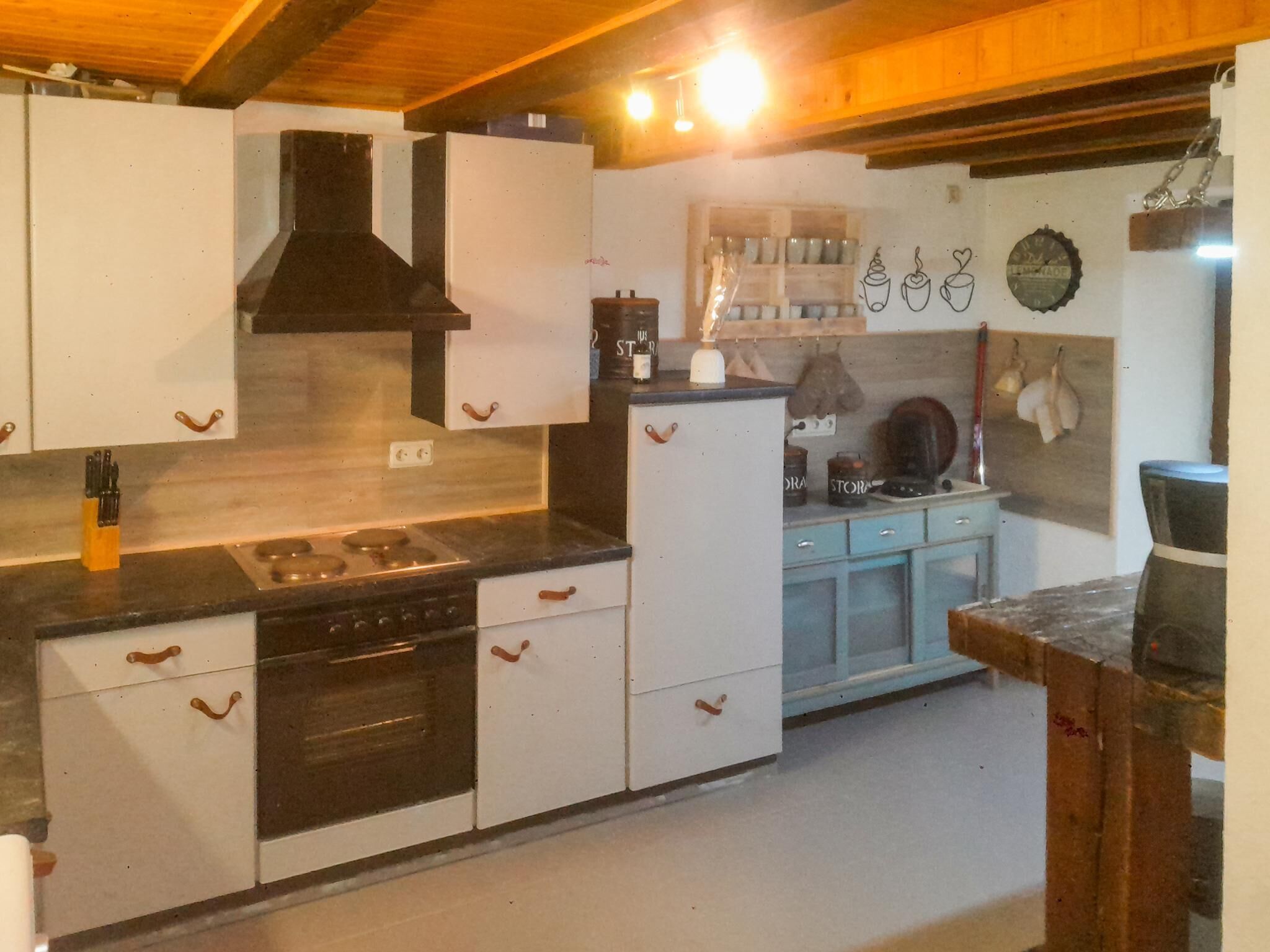 Eine kleine Küche mit weißen Schränken, einer schwarzen Dunstabzugshaube, einem Herd und einem Kühlschrank.