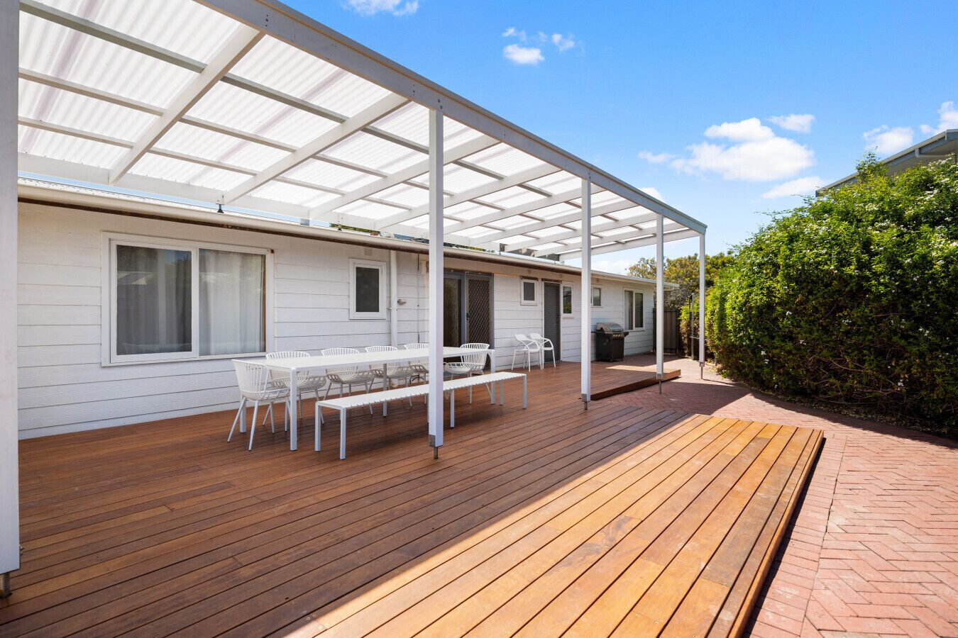 Une terrasse couverte avec une plateforme en bois, des chaises blanches et une table.