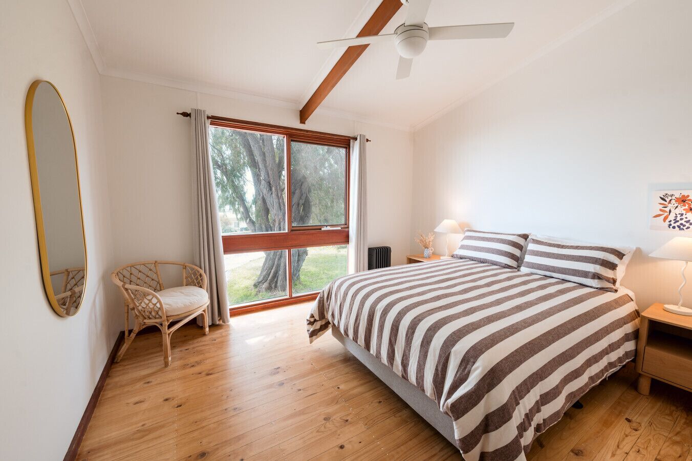 Een slaapkamer met een groot bed, een stoel, een plafondventilator en een raam met uitzicht op bomen.