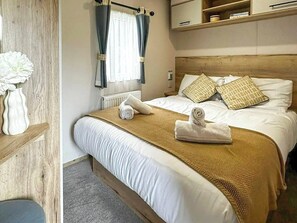 Une chambre d’hôtel avec un lit, des oreillers, une table de chevet, un vase avec des fleurs et une fenêtre avec des rideaux.