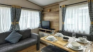 Un interior acogedor con un sofá, una mesa de comedor para dos personas, un televisor y cortinas.