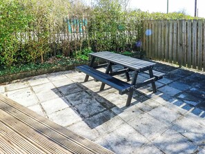 Una mesa de picnic en un patio empedrado, con una cerca de madera y follaje al fondo.