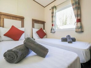 Dos camas individuales con almohadas rojas, una ventana con cortinas y toallas enrolladas sobre las camas.