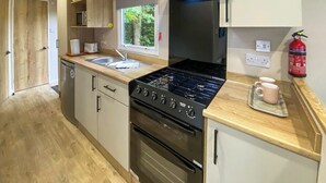 Une cuisine de taille réduite, équipée d’une cuisinière, d’un four, d’un évier et de meubles de rangement en bois.