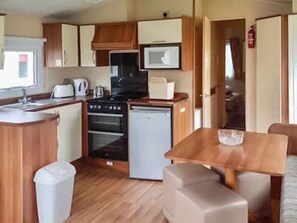 A compact kitchen with a stove, oven, microwave, and sink. There is a small dining area with a table and chairs. - Giltar 1 The Saltern Holiday Park - UKC8208 (Tenby)