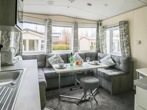 A compact kitchen with a dining area, a sink, and a window with curtains. - Giltar 1 The Saltern Holiday Park - UKC8208 (Tenby)