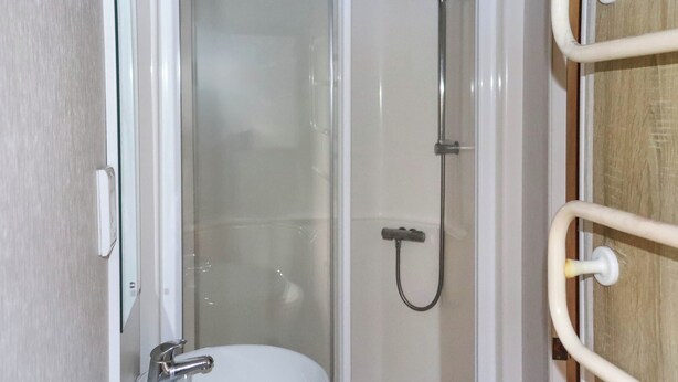 Een badkamer met een witte wastafel, een douchecabine van glas en een houten deur.