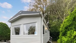 A small, single-story mobile home with a large window, a door, and a small porch. - Coastal 1 The Saltern Holiday Park - UKC8200 (Tenby)