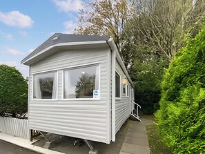 A small, single-story mobile home with a large window, a door, and a small porch. - Coastal 1 The Saltern Holiday Park - UKC8200 (Tenby)
