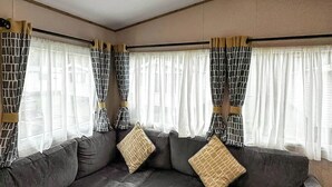 A corner sofa with patterned cushions, a window with sheer curtains, and a wooden beam ceiling. - Coastal 1 The Saltern Holiday Park - UKC8200 (Tenby)