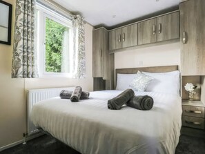 Une chambre à coucher avec un lit, une fenêtre avec des rideaux, un radiateur et une table de chevet sur laquelle se trouve un vase.