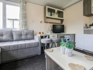 Ein kompakter Wohnraum mit einer Couch, einer kleinen Küchenzeile, einem Fernseher und einem Fenster mit Vorhängen.