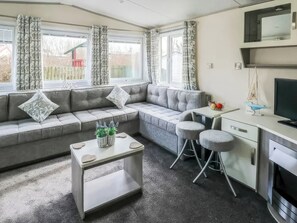 Un salon moderne avec un canapé gris, une petite table, un téléviseur et un coin cuisine équipé d’une cuisinière.
