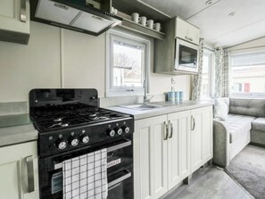 Une cuisine compacte équipée d’une cuisinière, d’un four et d’un évier. Il y a une fenêtre au-dessus de l’évier et un four à micro-ondes au-dessus de la cuisinière.