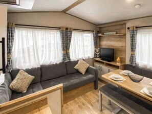 A compact living space with a sofa, a dining table, a television, and a cabinet. - Tenby 4 The Saltern Holiday Park - UKC8207 (Tenby)
