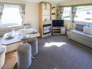 A furnished living room with a sofa, a TV, a dining table set, and a fireplace. - Tenby 4 The Saltern Holiday Park - UKC8207 (Tenby)