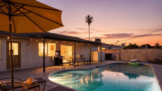 A swimming pool with lounge chairs and an umbrella, a barbecue area, and a view of the sunset.