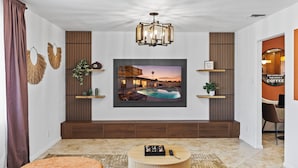 A modern living room with a large TV, a round coffee table, and a poolside view.