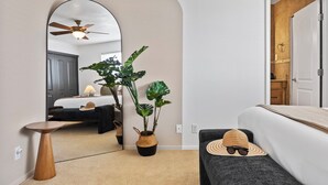 A hotel room with a bed, a small table, a mirror, a ceiling fan, and a potted plant.
