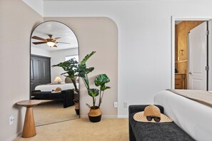 Habitación de hotel con cama, una mesita, espejo, ventilador de techo y una planta en maceta.