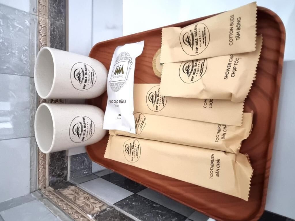 A tray with three white mugs and five brown paper bags labeled with hotel amenities.
