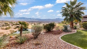 A landscaped garden with a variety of plants, a small pond, and a view of a distant town and mountains.
