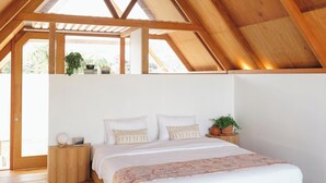 Ein Schlafzimmer mit Holzboden, einem Bett mit weißer Bettwäsche, einem kleinen Nachttisch und einer Topfpflanze.