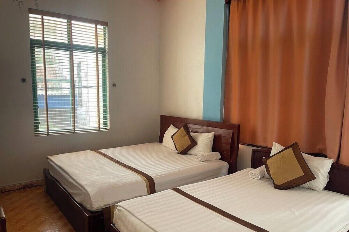 A hotel room with two beds, a window with blinds, a curtain, and a wooden floor.