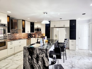 A modern kitchen with a marble island, stainless steel appliances, and a black chair.