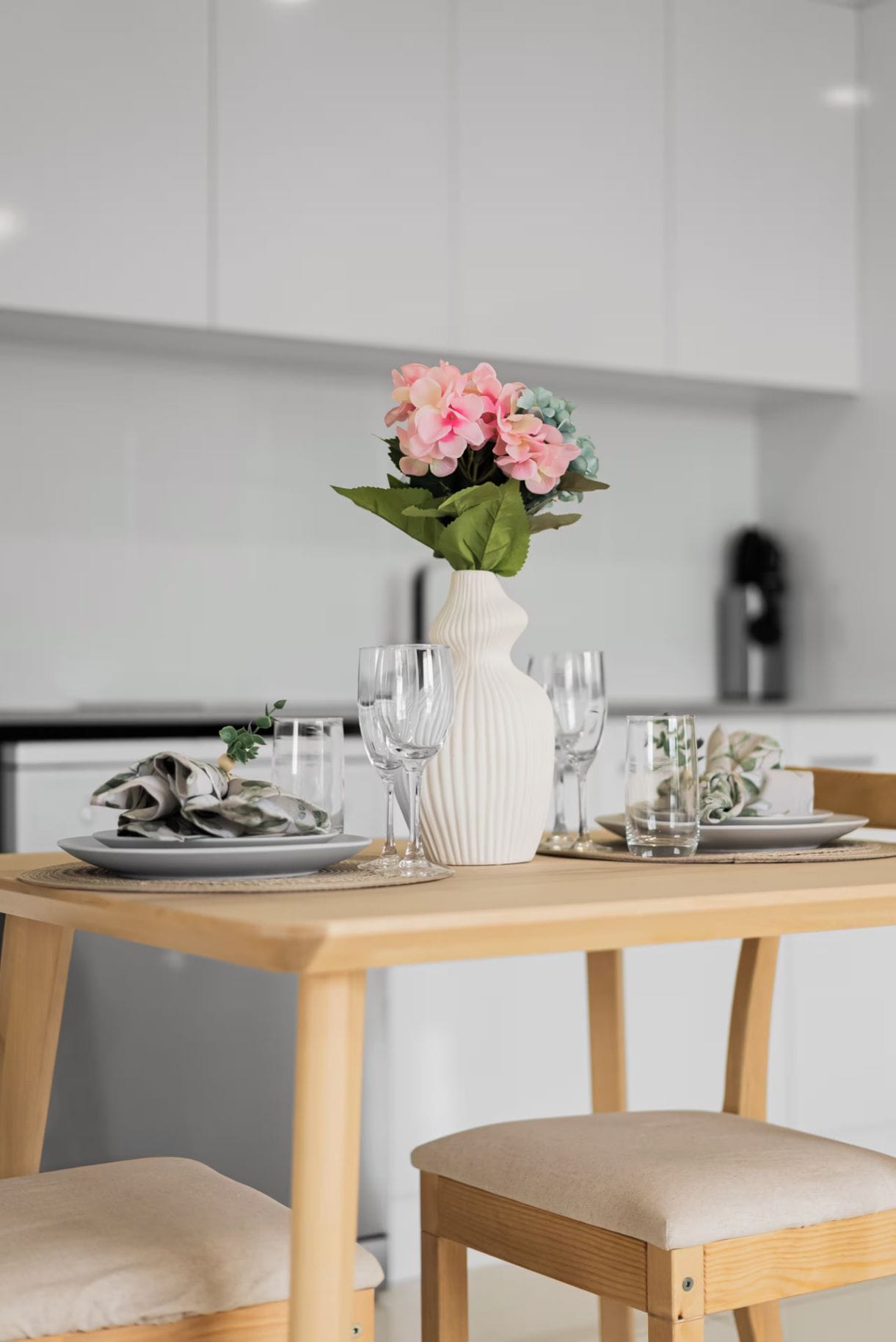 A dining table with a white vase, clear glasses, and a plate of food.