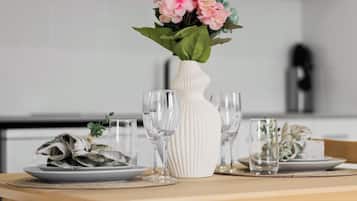 A dining table with a white vase, clear glasses, and a plate of food.