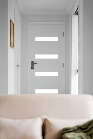 A hallway with a white door featuring horizontal slats, a framed picture on the left, and a sofa with a cushion in the foreground. - Scandi Calm - Sleek 1BD Duplex near Everything (Pimpama)