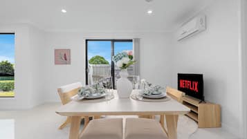 A modern dining area with a wooden table, chairs, and a television displaying 'NETFLIX'.