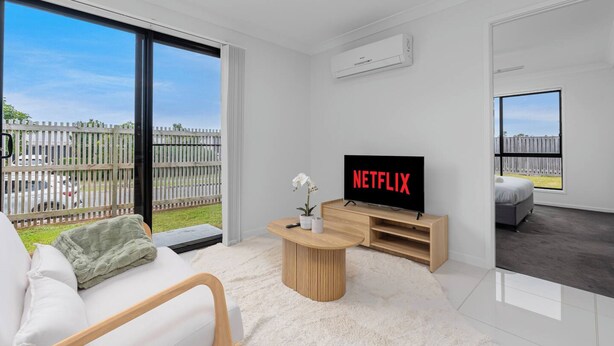 Moderni olohuone, jossa on litteänäyttöinen televisio, jossa näkyy Netflix, sohva, sohvapöytä ja näkymä aidatulle ulkoalueelle.