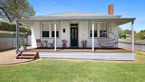 A single-story house with a covered porch, a swing chair, and a small outdoor seating area.