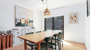 A dining area with a wooden table and green chairs, a hanging light fixture, and artwork on the walls.