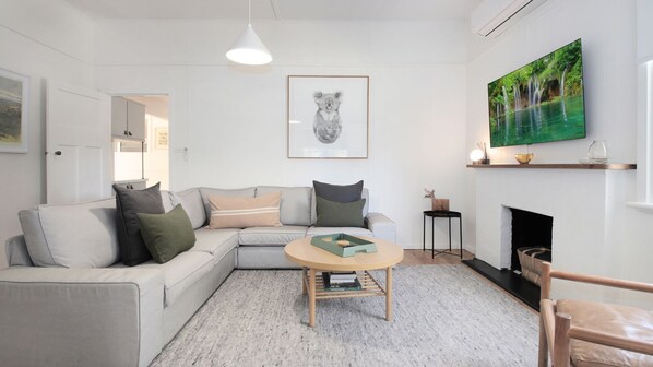 A modern living room with a grey sofa, a round wooden coffee table, a framed koala artwork, and a large green nature painting on the wall. - The Gums, Beechworth (Beechworth)