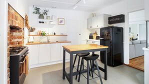 A modern kitchen with white cabinets, a brick wall, a wooden table, and a black refrigerator.