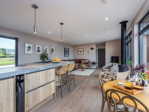 A modern kitchen with a central island, a dining area with a wooden table and chairs, and a living space with a sofa and a fireplace. - The Granary - UK48622 (Rachel&rsquo;s Farm)