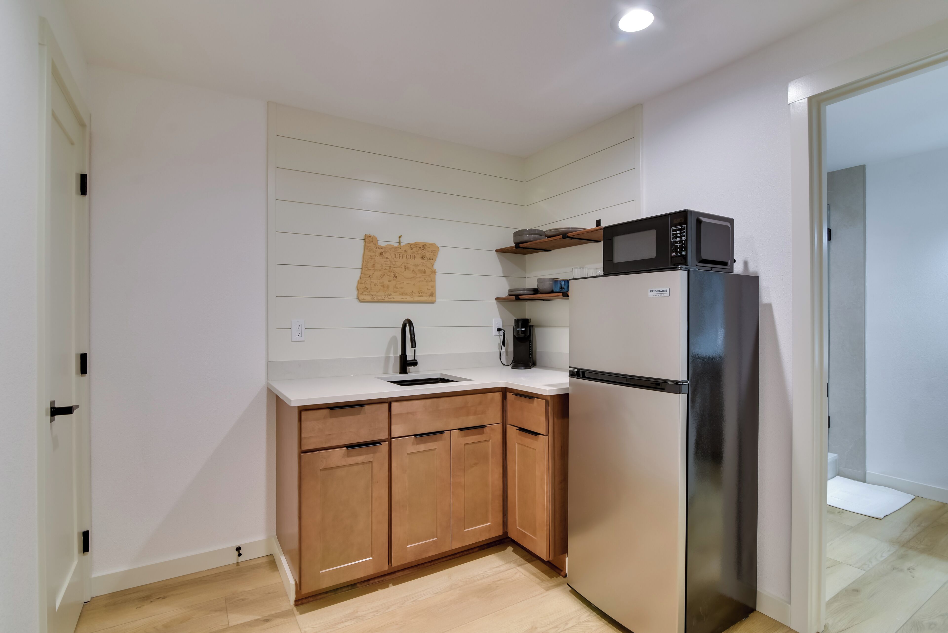 A compact kitchen with wooden cabinets, a stainless steel refrigerator, a microwave, and a coffee maker.